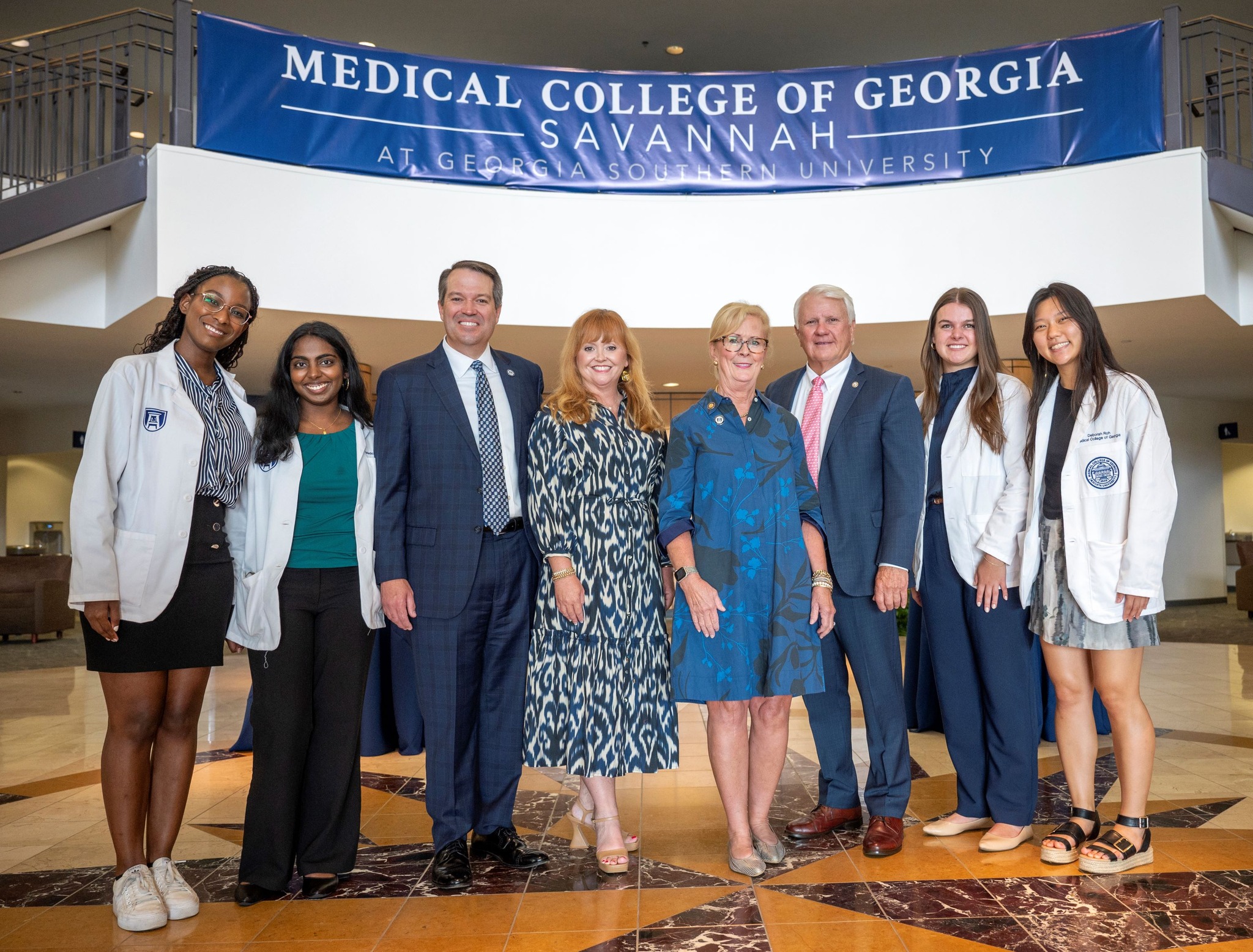 A group of medical students and professionals pose together at the Medical College of Georgia Savannah campus at Georgia Southern University, standing under a banner celebrating the institution.